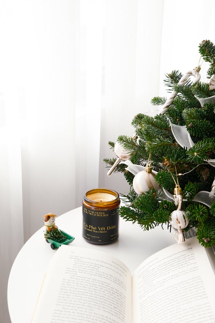 Festive candle beside a decorated fir tree on a round white table, capturing a holiday ambiance.