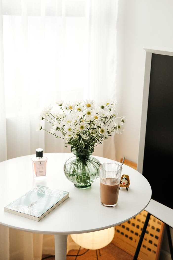 A minimalist setup with white daisies, perfume, and coffee on a round table.